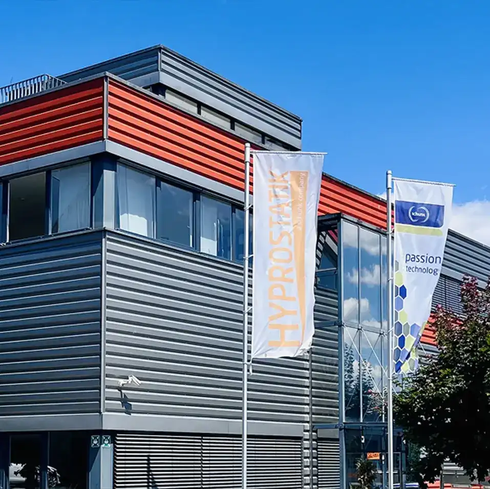 Firmengebäude der HYPROSTATIK Schönfeld GmbH in Göppingen mit Unternehmensflaggen vor modernem Industriegebäude.